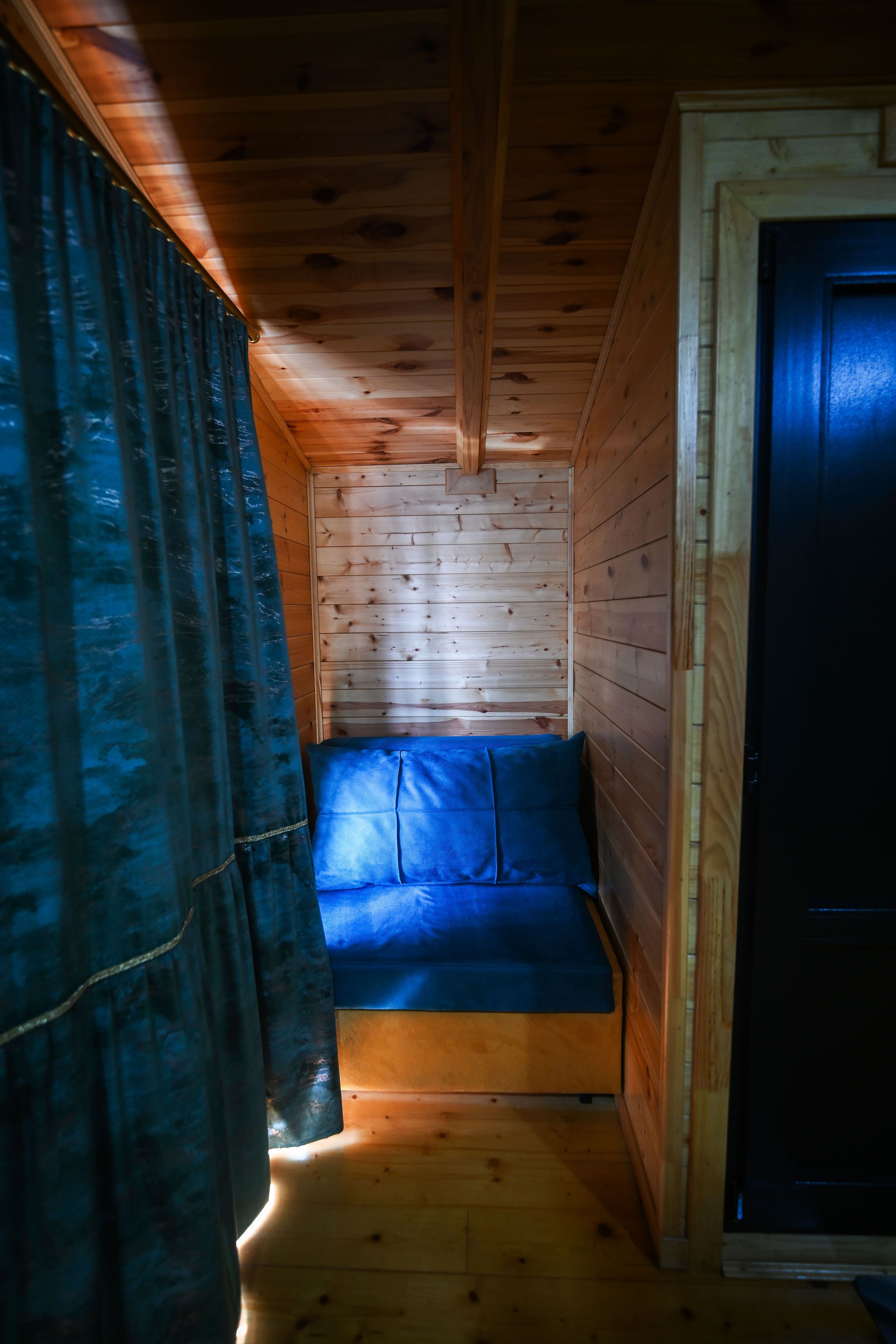 En stuga med träpanel i taket, en blå soffa och en dörr.