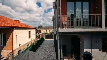 A courtyard with a stone floor, a tree with a metal bucket, and a building with a balcony.