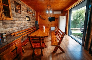 Interior de madera con una larga mesa de comedor, bancos, paredes de piedra y vistas a través de un ventanal.