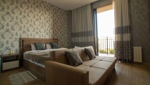 A bedroom with a large bed, a sofa, a nightstand, and a window with curtains. - Prestige Guest House (Kutaisi)