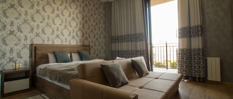 Un dormitorio con una cama grande, un sofá, una mesita de noche y una ventana con cortinas.