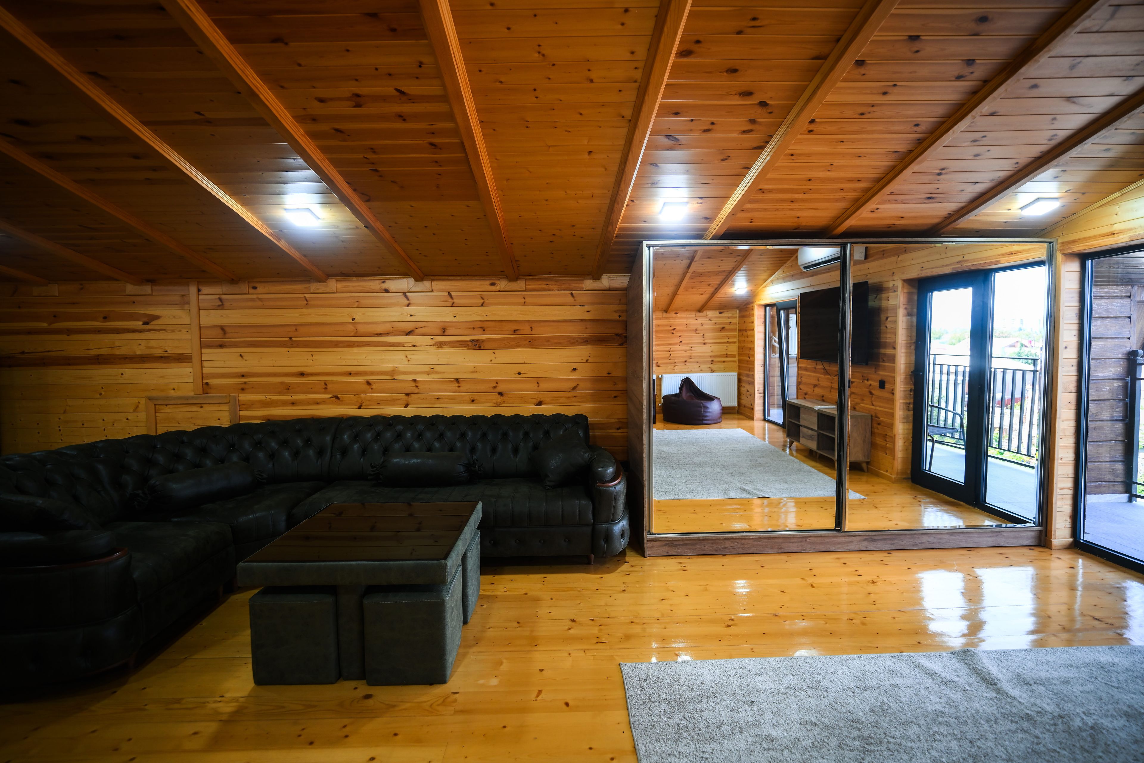 A wooden interior with a black leather sofa, a small coffee table, and a glass door leading outside.