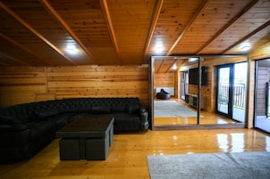 Een houten interieur met een zwarte leren bank, een klein bijzettafeltje en een glazen deur naar buiten.