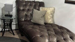 A room with a brown tufted sofa, a small glass table with a lamp, and a mirror on the wall. - AMAZING PRIVATE QUIET & COMFORTABLE SHORT STAYS!! 
KING SZ BED.10 mins from JFK (Queens)
