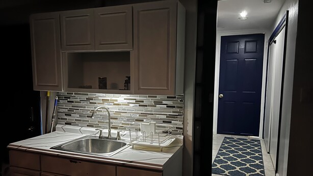 A kitchen with a stainless steel sink, a tiled backsplash, and light-colored cabinets. - AMAZING PRIVATE QUIET & COMFORTABLE SHORT STAYS!! 
KING SZ BED.10 mins from JFK (Queens)