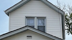 A two-story house with a blue front door, a number '15019' above the door, a covered porch with a white railing, and a brick foundation. - AMAZING PRIVATE QUIET & COMFORTABLE SHORT STAYS!! 
KING SZ BED.10 mins from JFK (Queens)