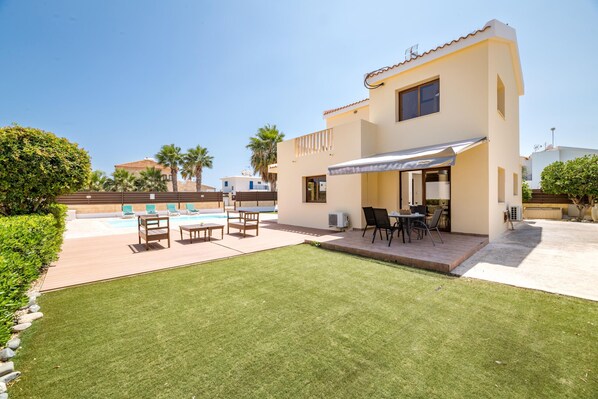 Una casa moderna de dos plantas con un patio, mobiliario exterior y una piscina.