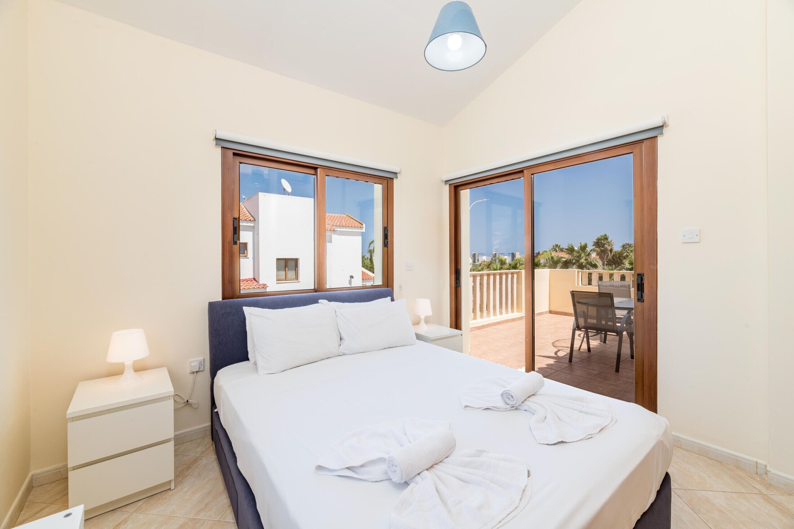 Ein Hotelzimmer mit Bett, Nachttisch, Lampe und Blick auf den Außenbalkon.