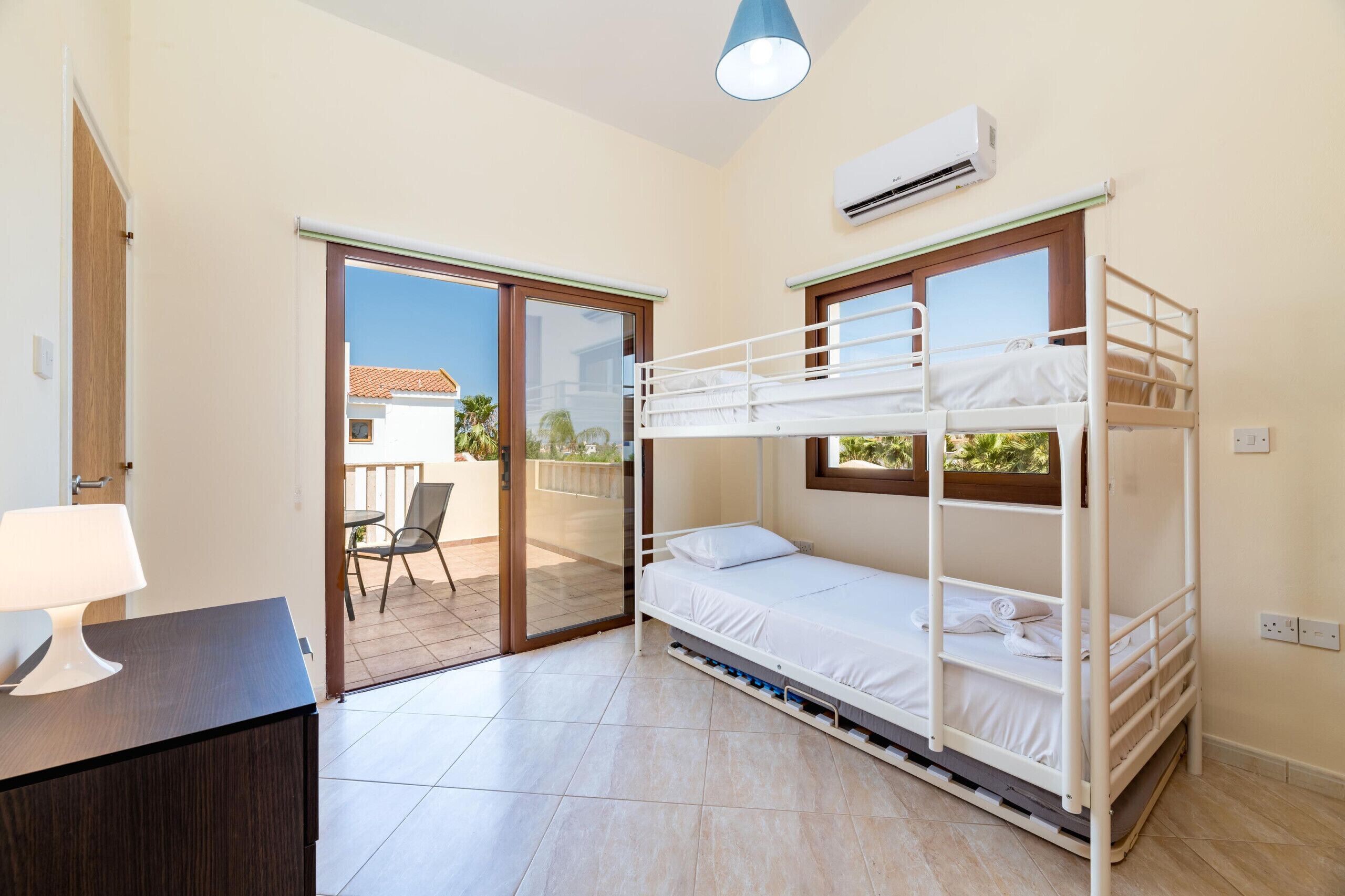A bedroom with a bunk bed, a desk with a lamp, and a sliding glass door leading to a balcony.