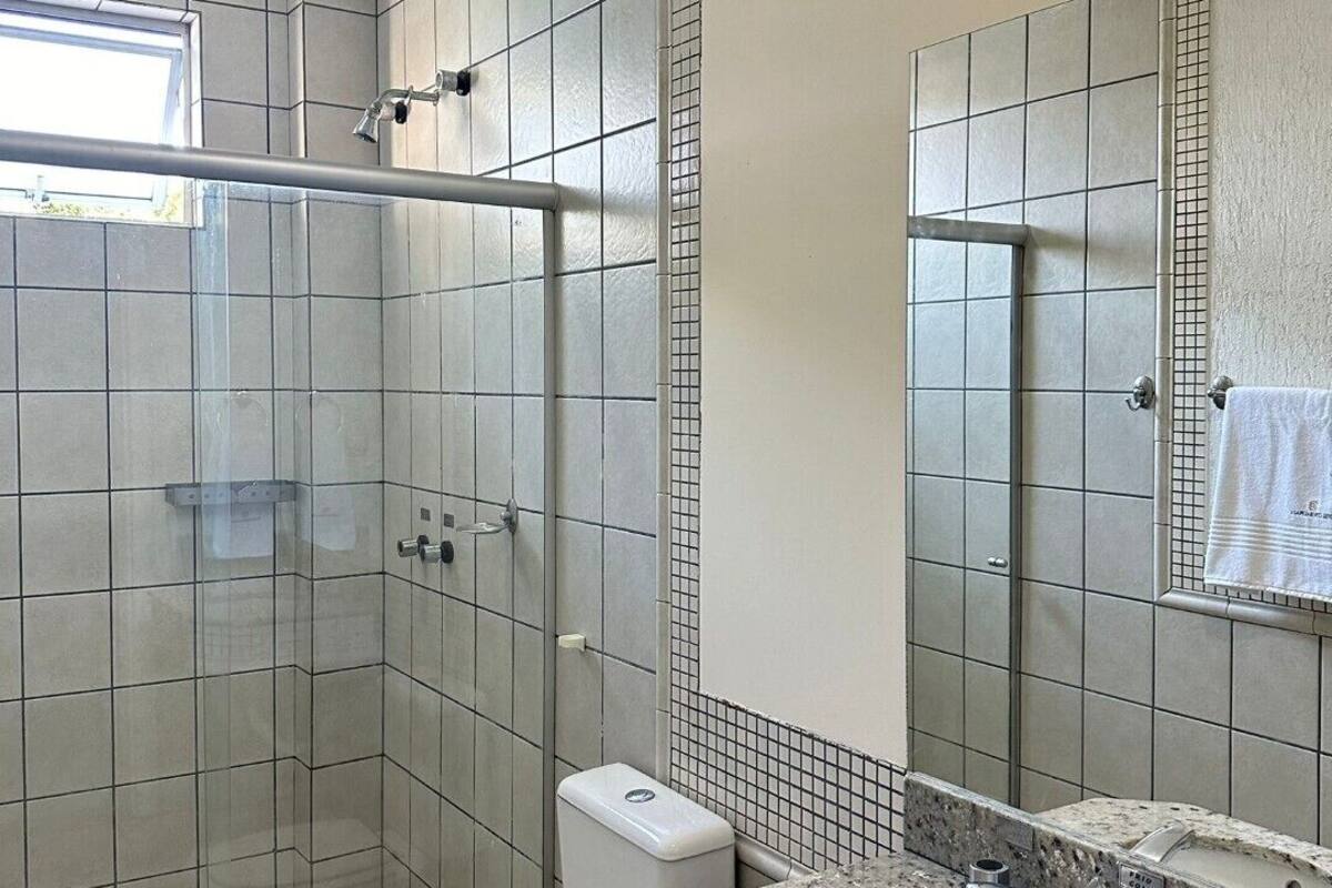 A bathroom with a glass-enclosed shower, a toilet, and a sink with a mirror.