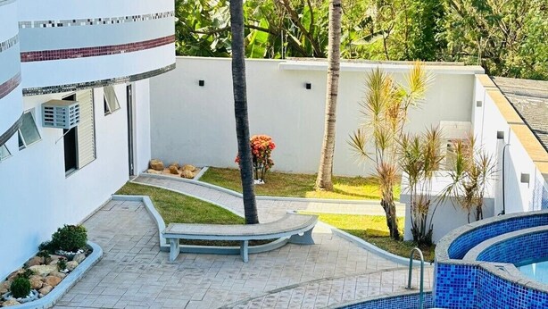 Un área de piscina moderna con una piscina de color azul cristalino, un suelo de baldosas y un pequeño jardín con palmeras.
