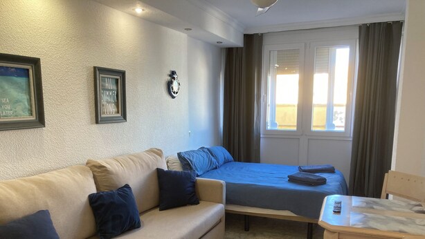 A room with a sofa, a bed, a small table, and a chair. There are two windows with curtains, a wall clock, and two framed pictures. - Benalmadena Beach Studio, Double bed, En Suite.  (Benalmádena)