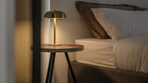 A bedroom with a bed, a bedside table with a lamp, and a wooden floor.