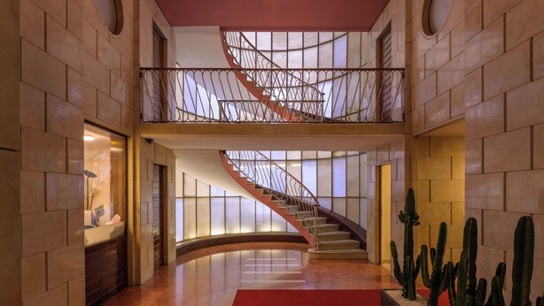 A spacious lobby with a curved staircase, a red carpet, and a cactus display.