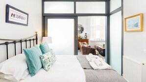 Quarto de hotel com cama, escrivaninha, cadeira, cômoda e uma janela grande.
