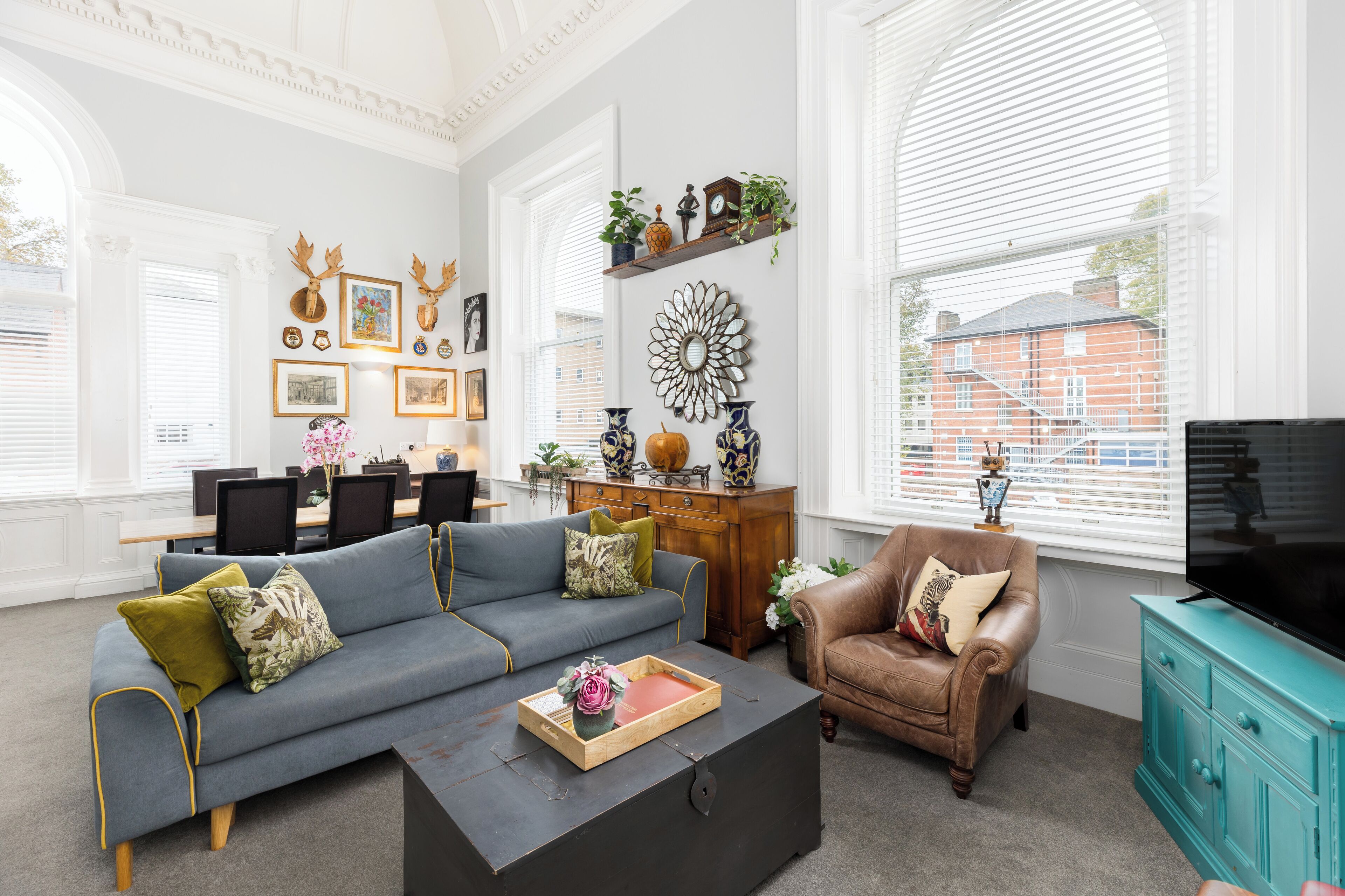 A spacious living room with a sectional sofa, a coffee table, a leather armchair, and a television on a teal cabinet.