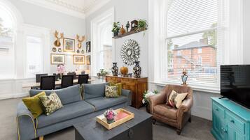 A spacious living room with a sectional sofa, a coffee table, a leather armchair, and a television on a teal cabinet.