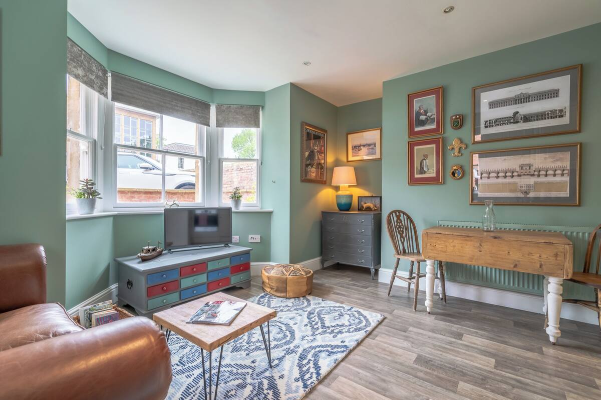 A cozy living room with a television, a wooden bench, a table, and a patterned rug.