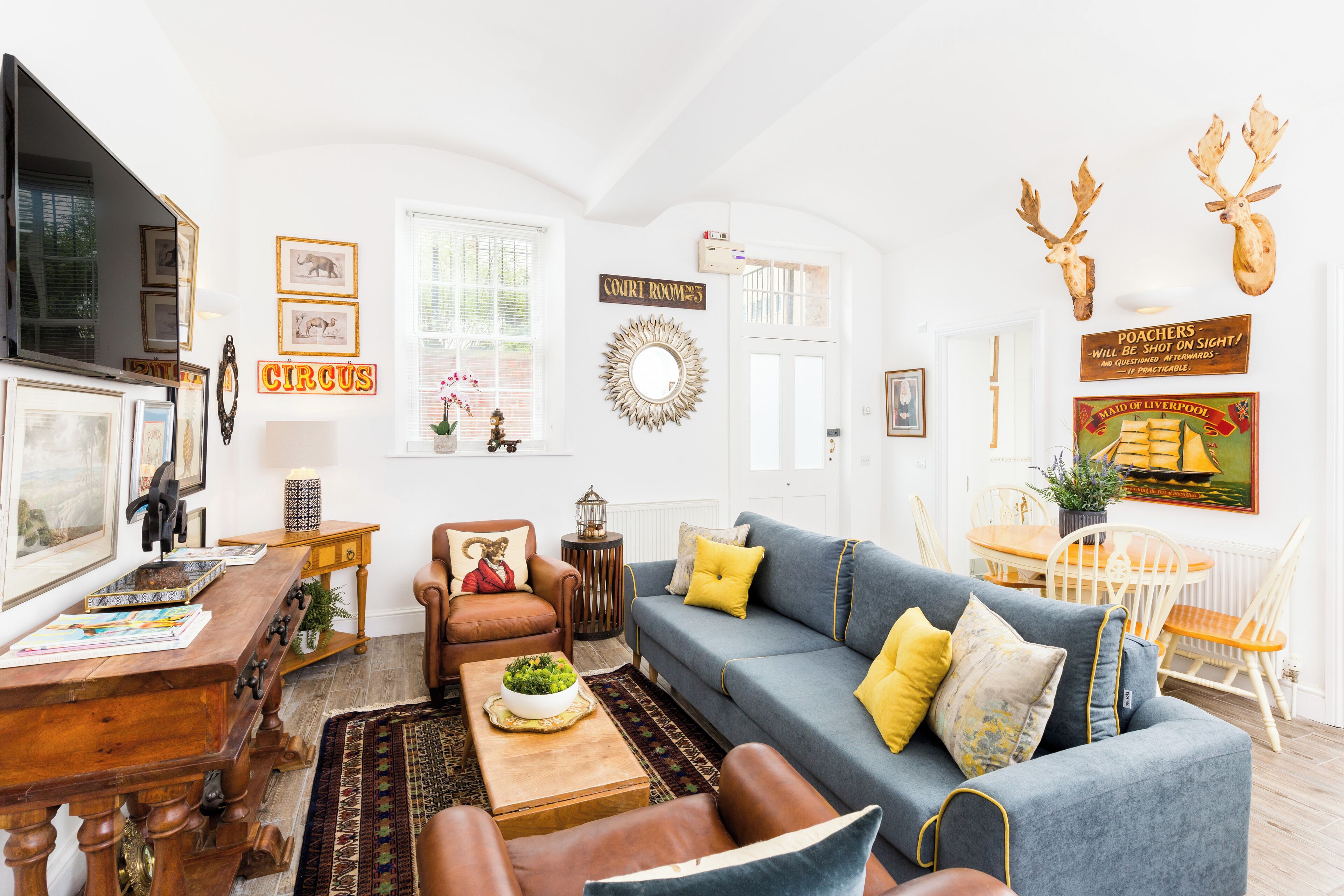 A living room with a blue sofa, wooden coffee table, and a fireplace. There are framed pictures on the walls and a sign that says "Court Room".