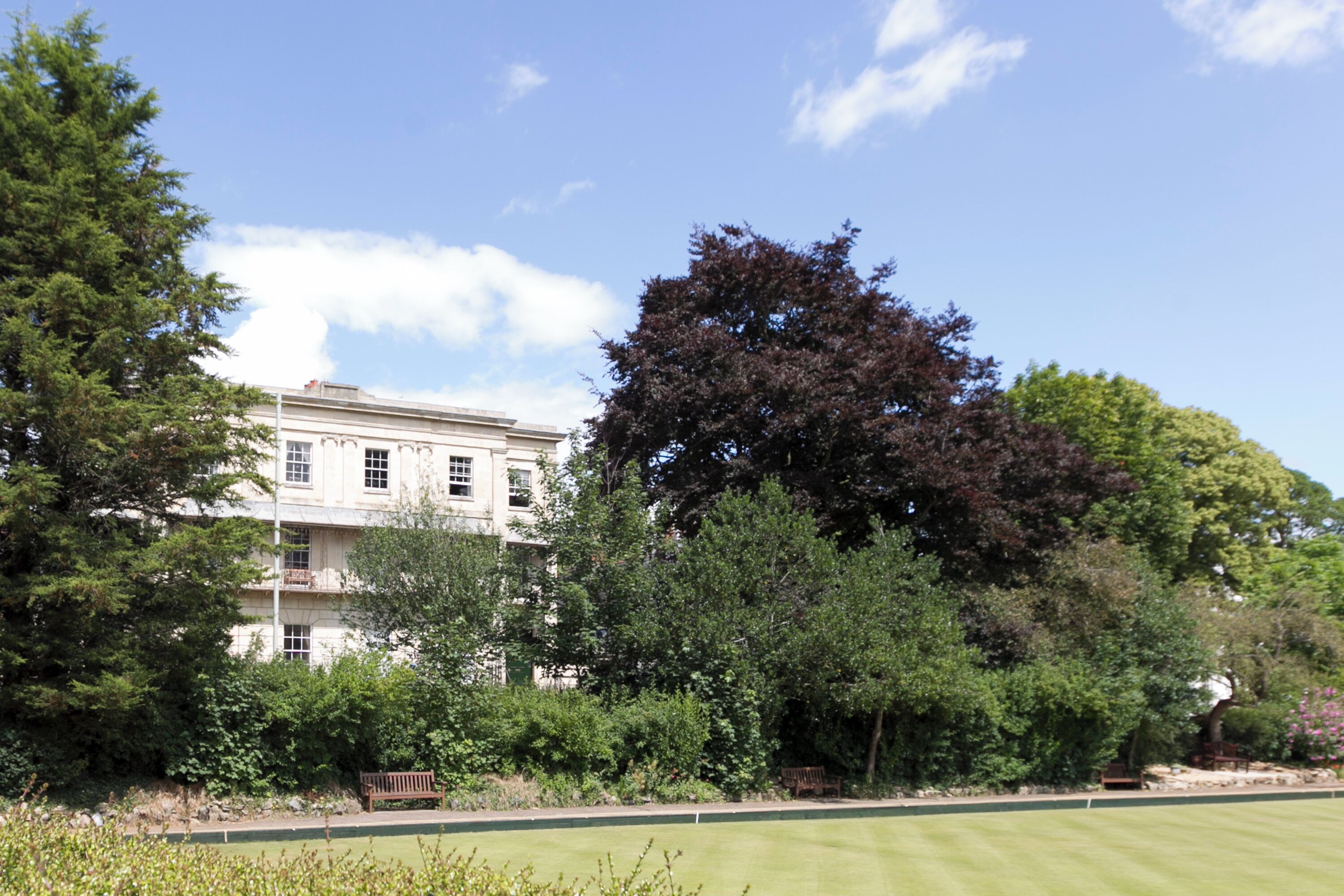 A building with a large lawn in front, surrounded by trees and a bench.