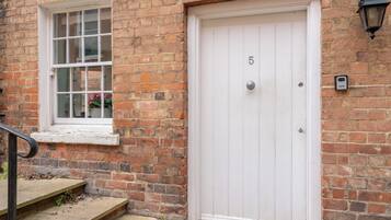 A white door with the number 5, a brick wall, a window with a white frame, and a small step leading to the door.
