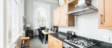 Een moderne keuken met houten kastjes, een gasfornuis en een eethoek met een tafel en stoelen.