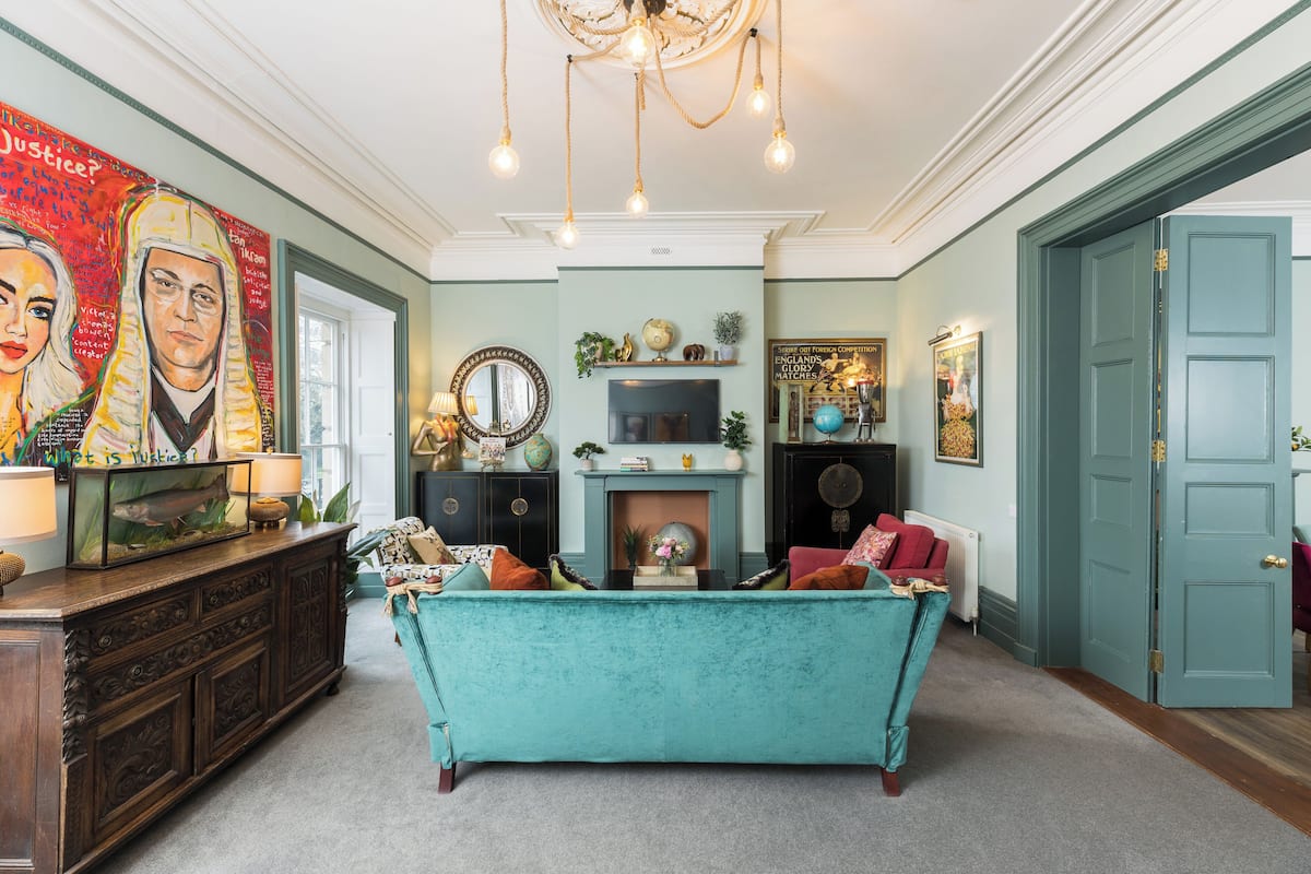 A spacious living room with a teal sofa, a fireplace, and a large painting on the wall.