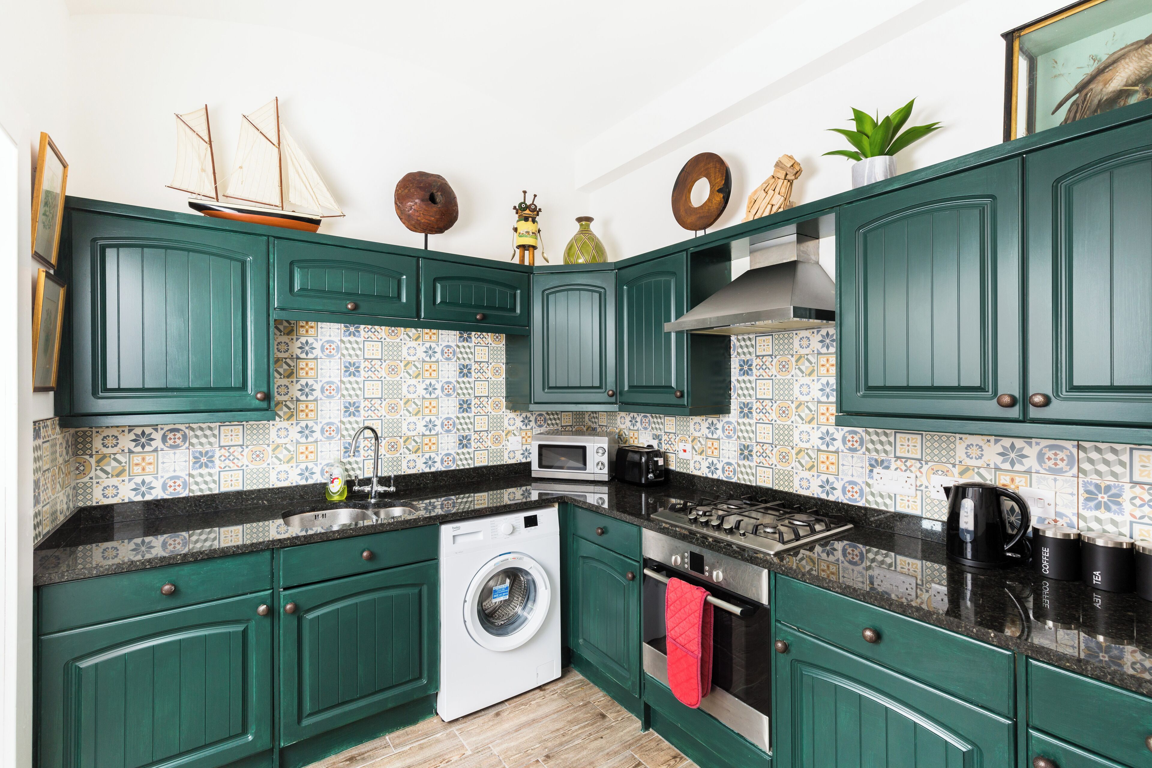 A kitchen with green cabinets, a washing machine, a microwave, and a stove.