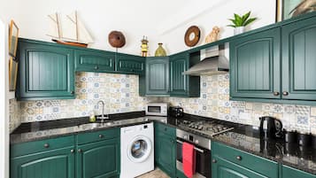 A kitchen with green cabinets, a washing machine, a microwave, and a stove.