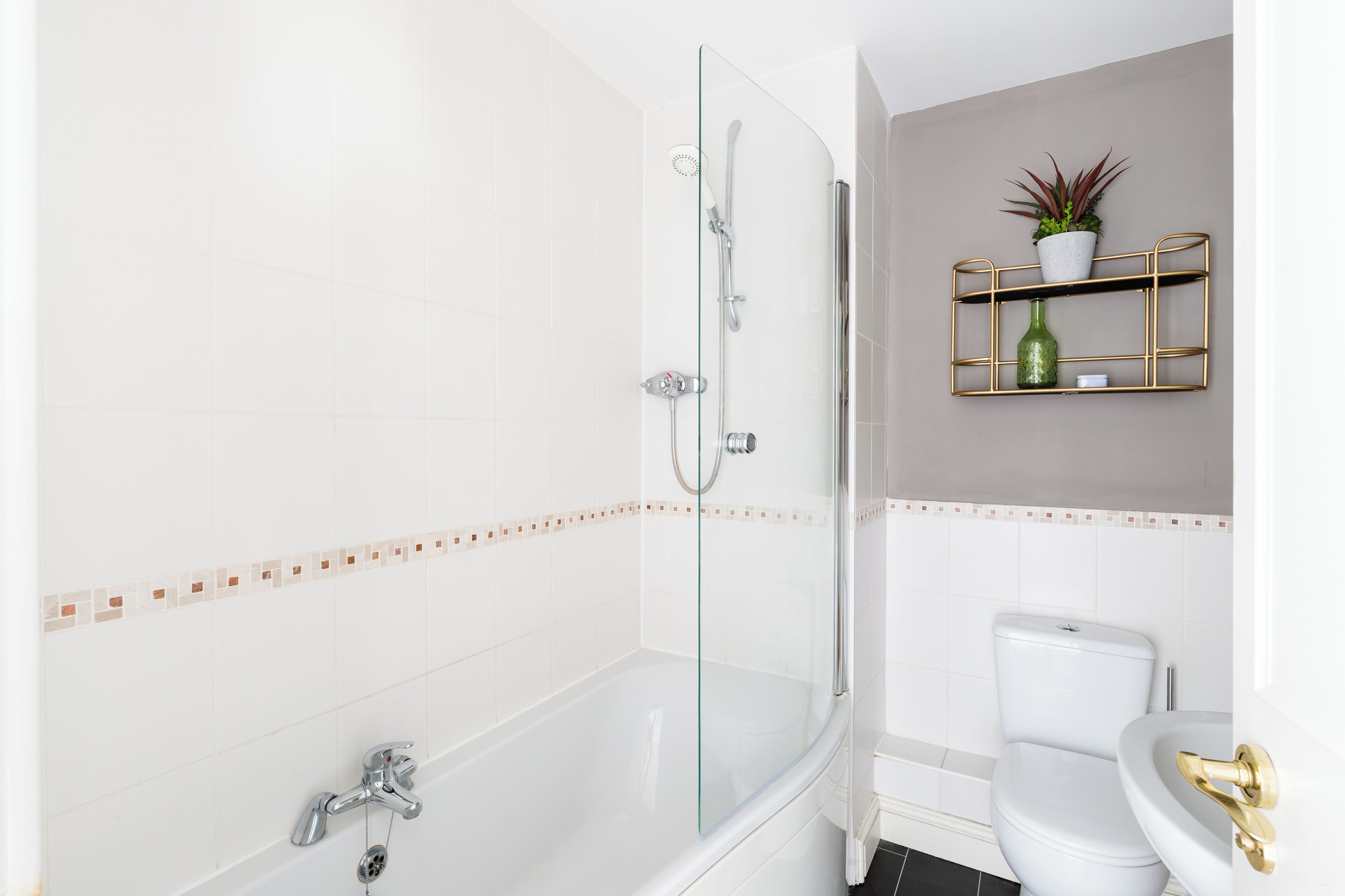 A modern bathroom with a glass-enclosed shower, a white bathtub, a toilet, and a sink with gold fixtures.