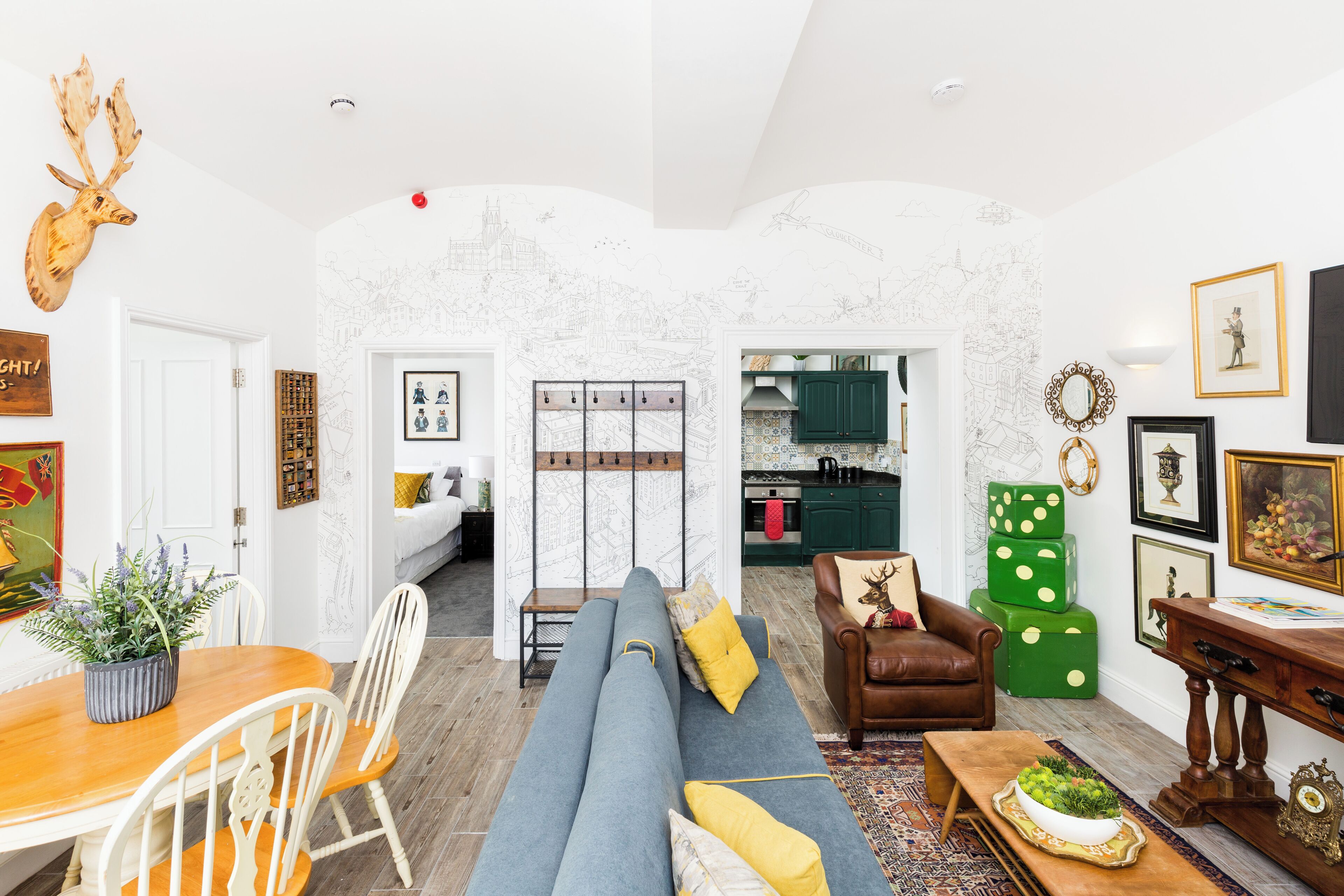 Ein Wohnzimmer mit einer Couch, Sesseln, einem Esstisch und einer Küche im Hintergrund.