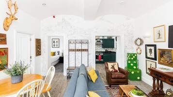 Ein Wohnzimmer mit einer Couch, Sesseln, einem Esstisch und einer Küche im Hintergrund.