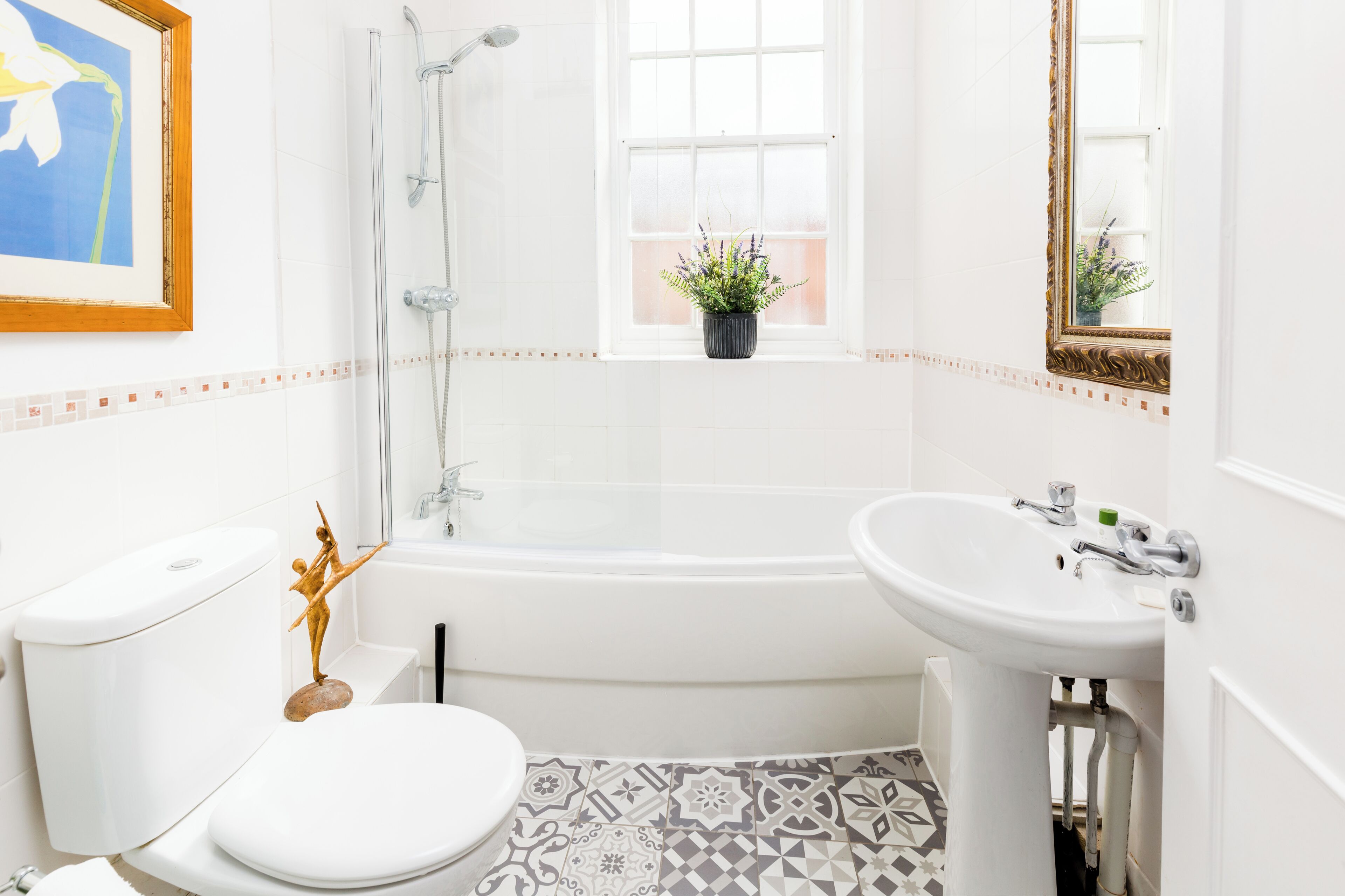 A bathroom with a toilet, sink, bathtub, shower, and a window with a plant.