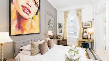 Una habitación de hotel elegante y bien equipada con una cama grande, un área de estar con una silla, un tocador con espejo y un cuadro de gran tamaño en la pared.