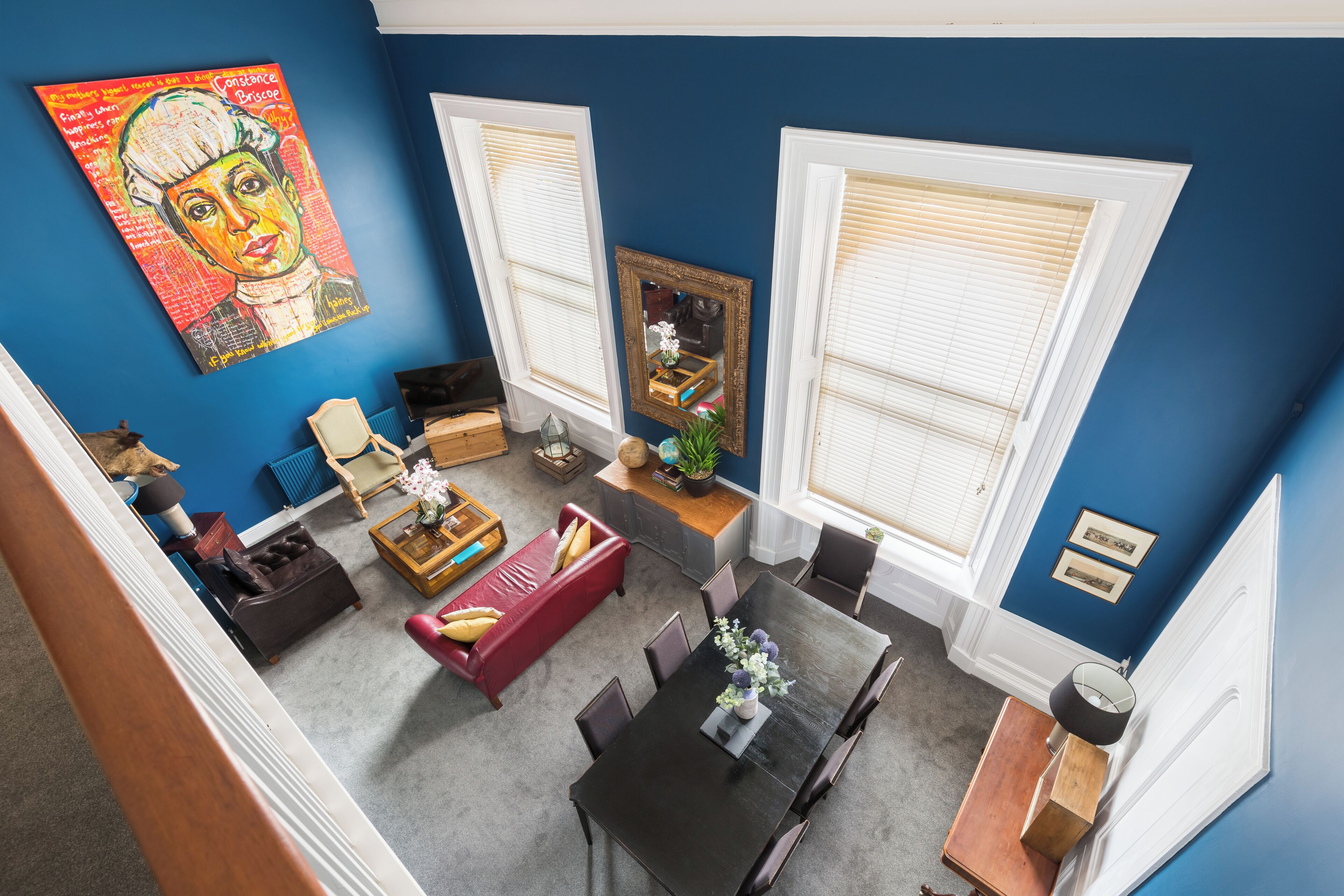 A living room with a blue wall, a red sofa, a dining table with chairs, and a painting.