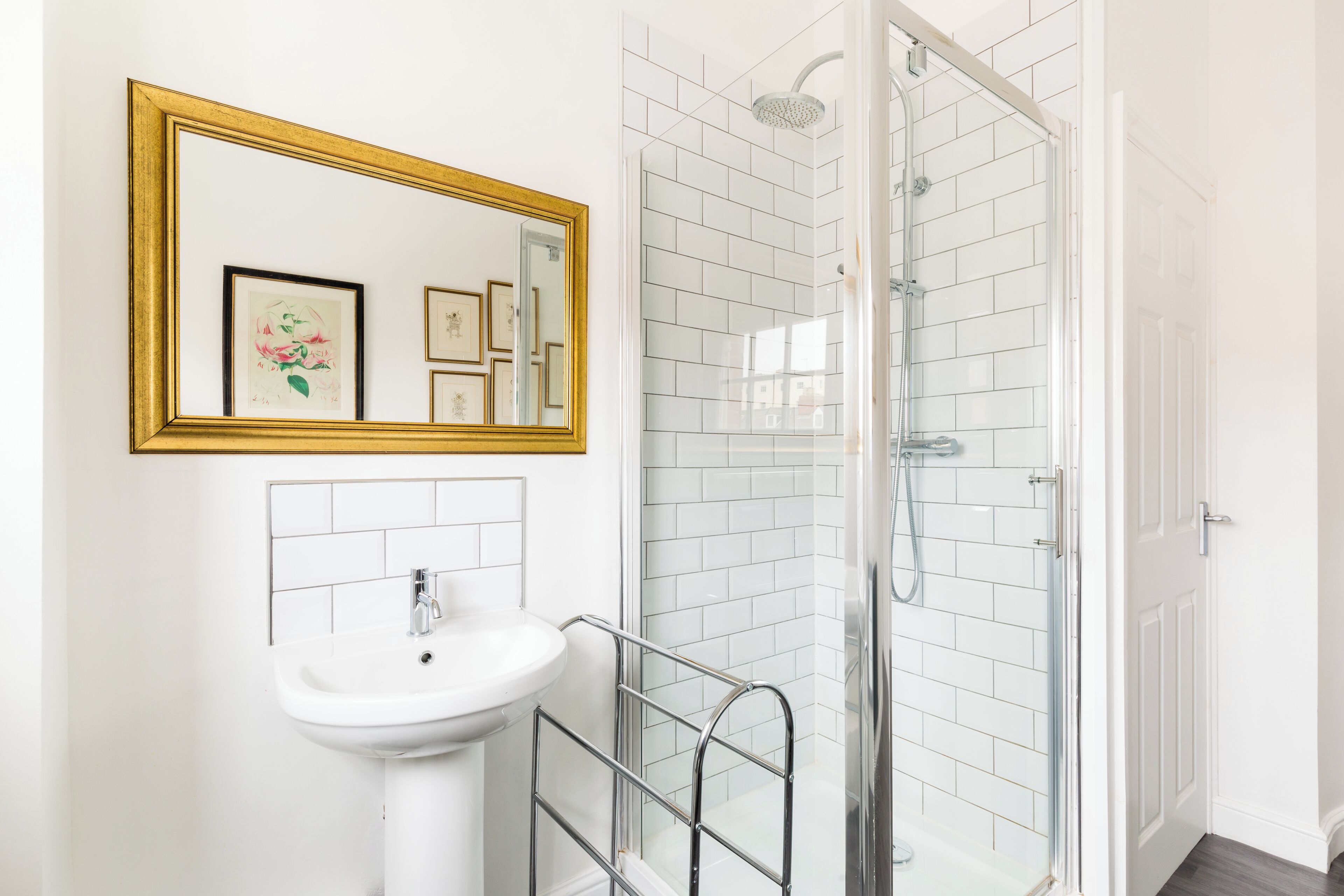 A bathroom with a white sink, a mirror with a gold frame, and a glass shower enclosure.
