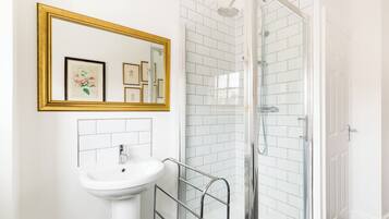 Un baño con lavamanos blanco, un espejo con marco dorado y cabina de ducha de vidrio.