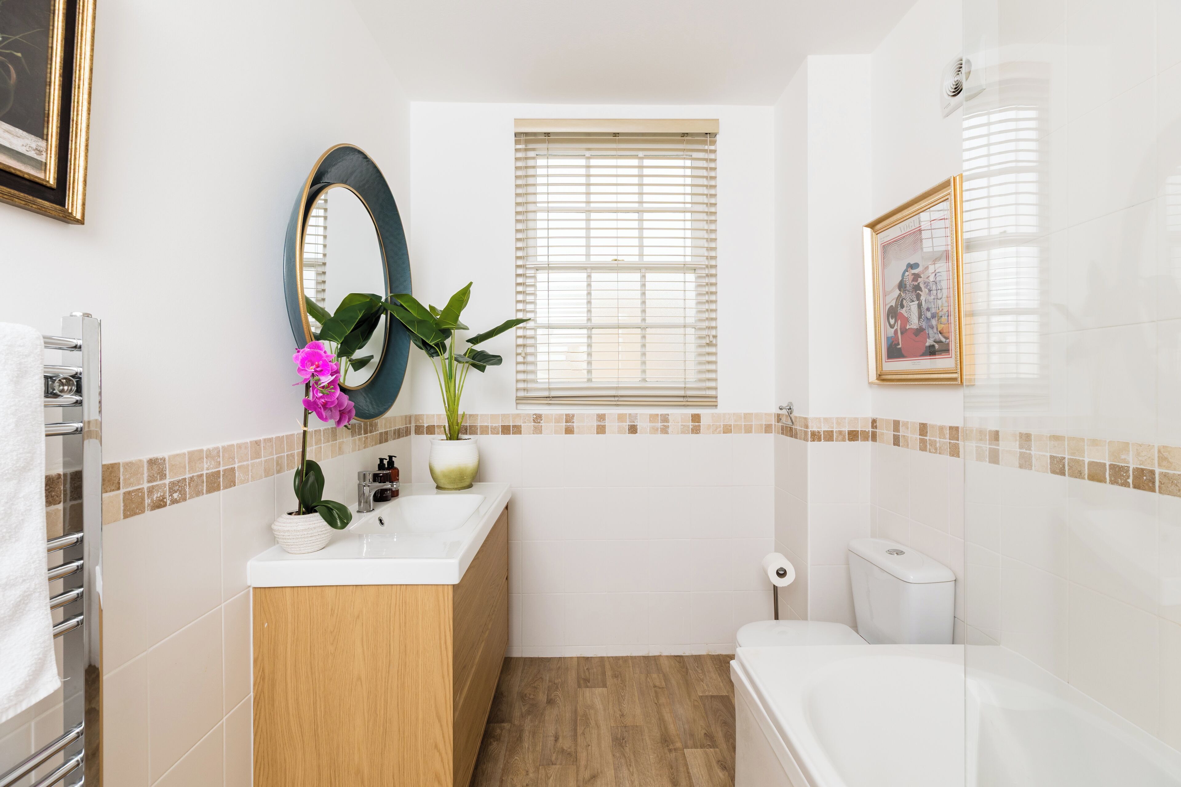 Une salle de bain avec un meuble-lavabo en bois, un évier, un miroir, des toilettes et une fenêtre avec des stores.