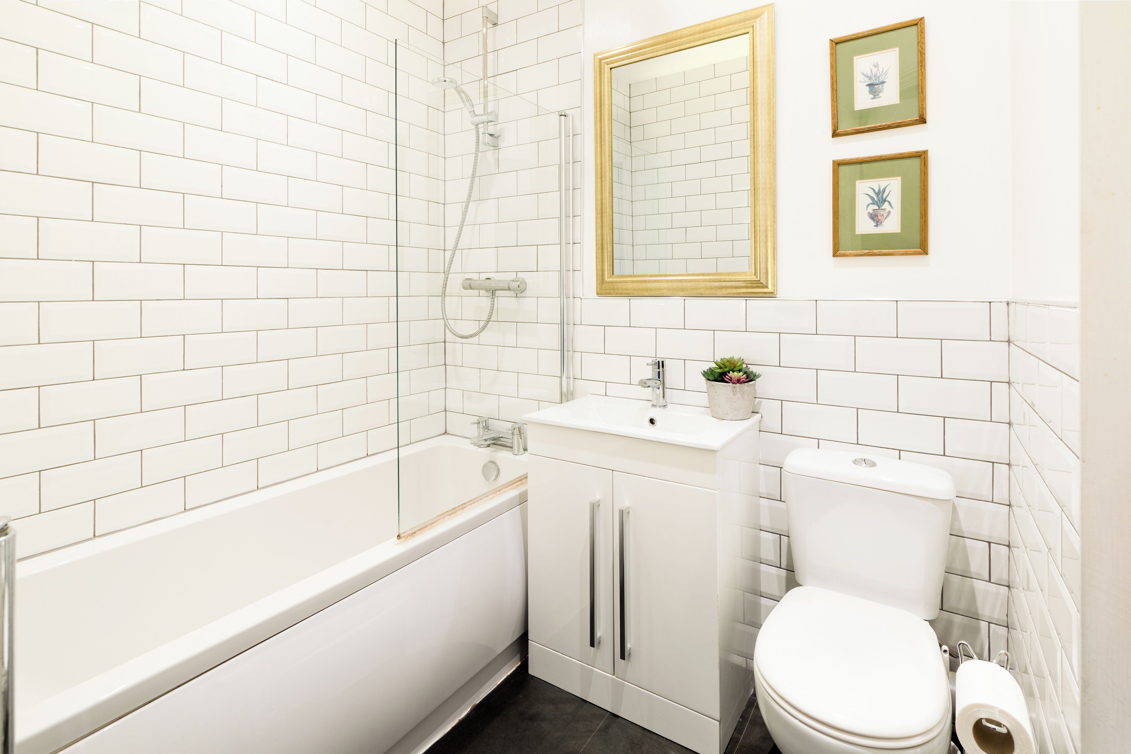 Une salle de bain avec une baignoire blanche, un lavabo et des toilettes. Des tableaux encadrés ornent le mur.