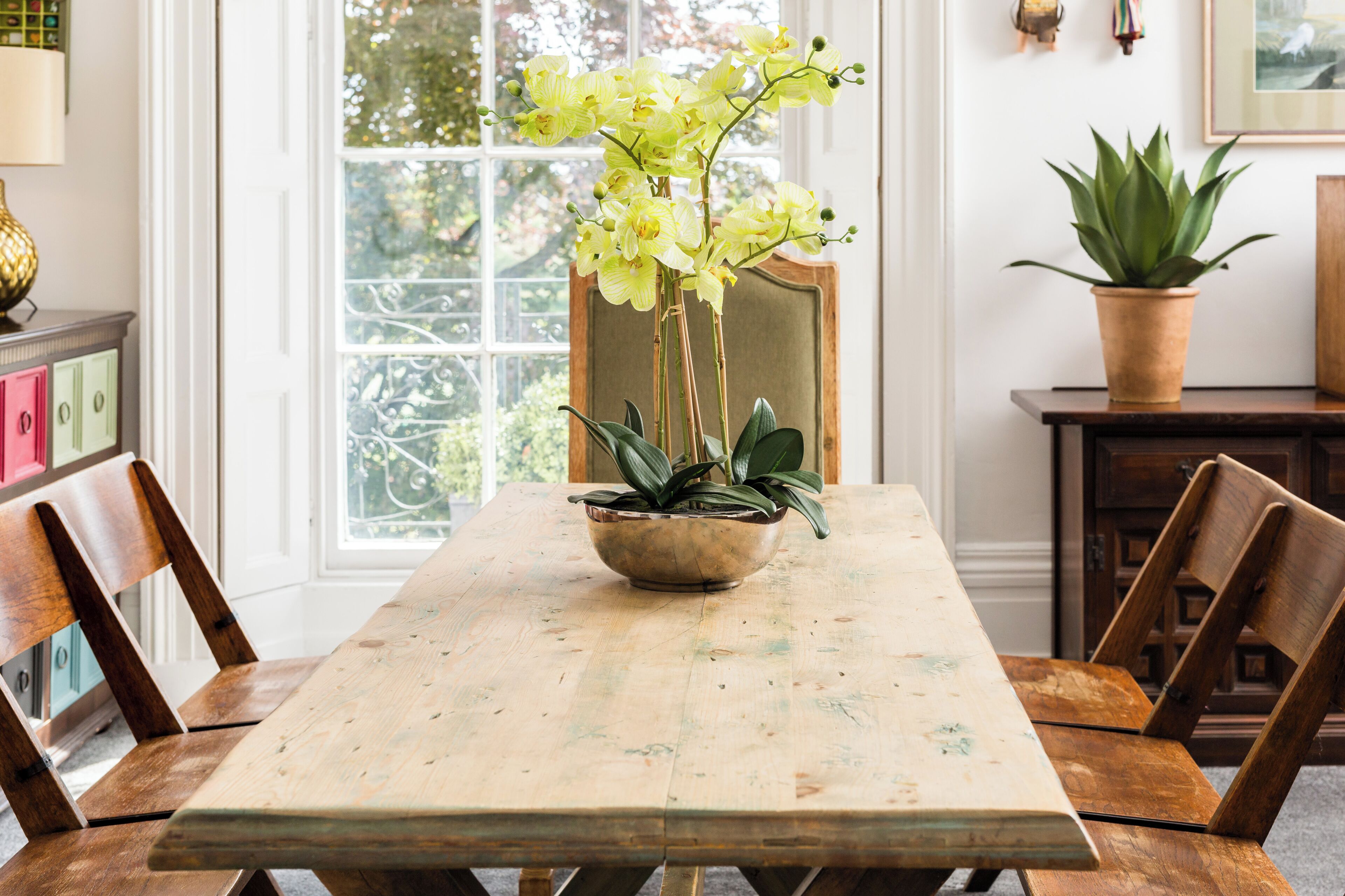 Una mesa de comedor de madera con un jarrón de flores, sillas de madera y una ventana con vistas al verdor.