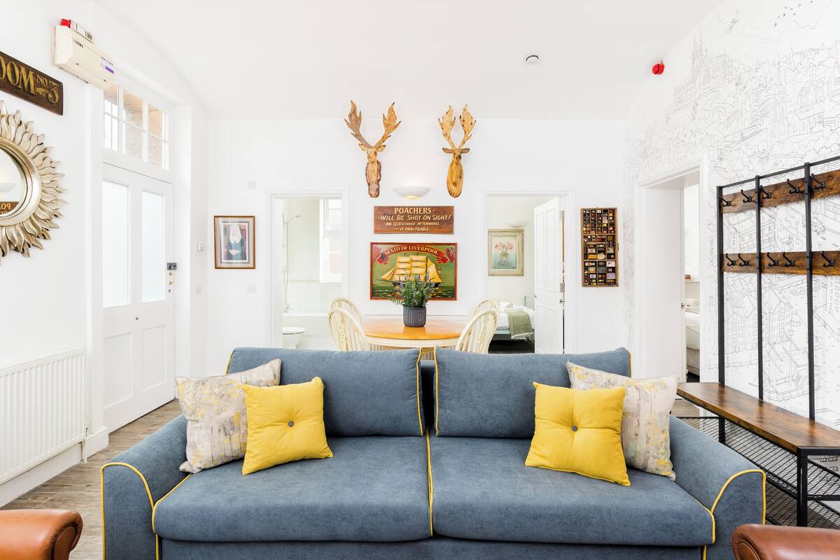 A modern living room with a blue sofa, yellow cushions, and a dining area with a wooden table and chairs.