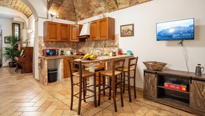 A kitchen with wooden cabinets, a tiled backsplash, a central island with stools, a television mounted on the wall, and a brick ceiling. - Domus Gelsomino, St Peter's Square, Vatican, Central Rome (Rome)