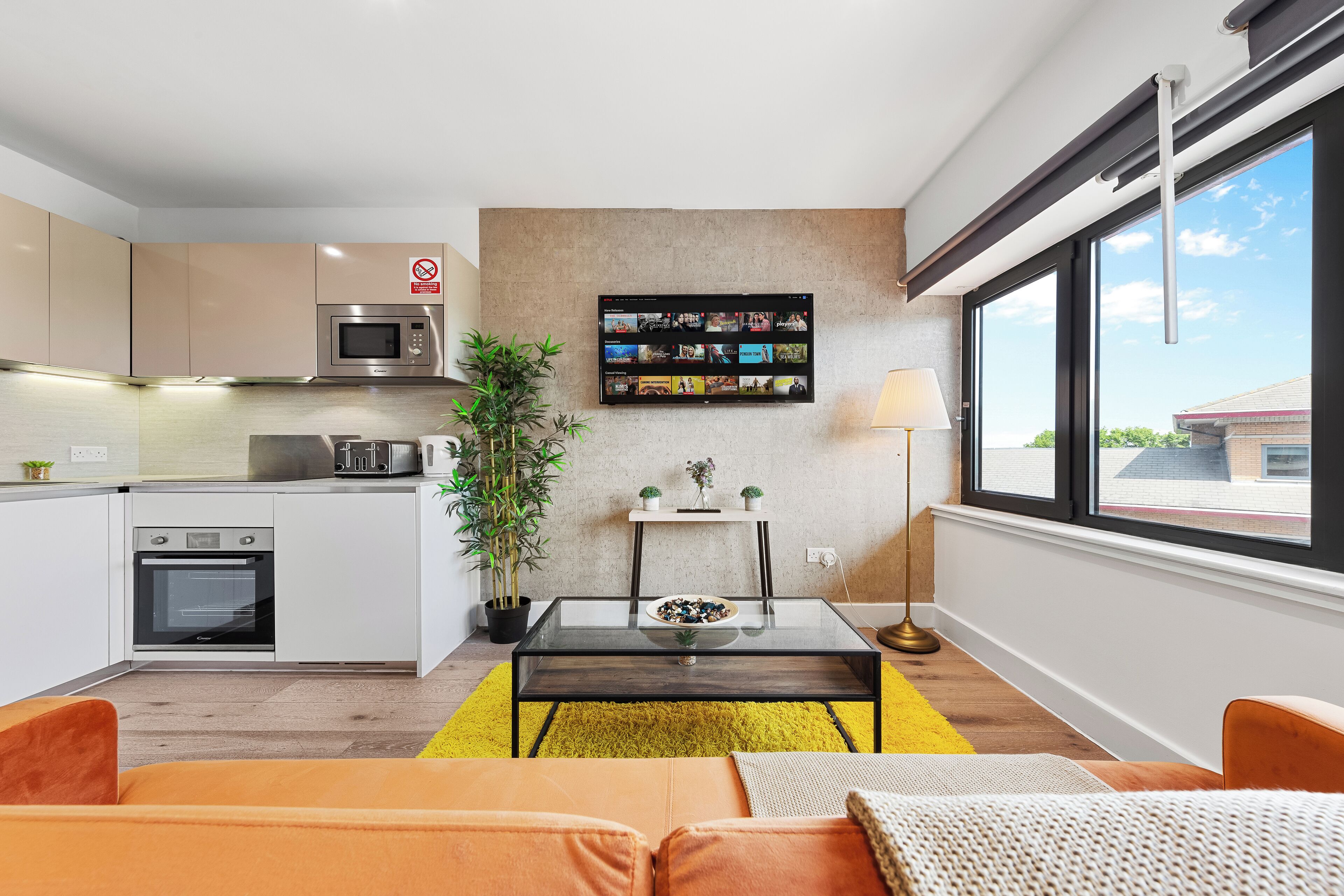 Eine moderne Küche mit Mikrowelle, Backofen und einem Essbereich mit Glastisch und gelbem Teppich.