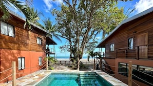A pool area with wooden cabins, clear blue water, and a view of the beach. - Mt. Plaisir Estate Hotel (Grande Riviere)