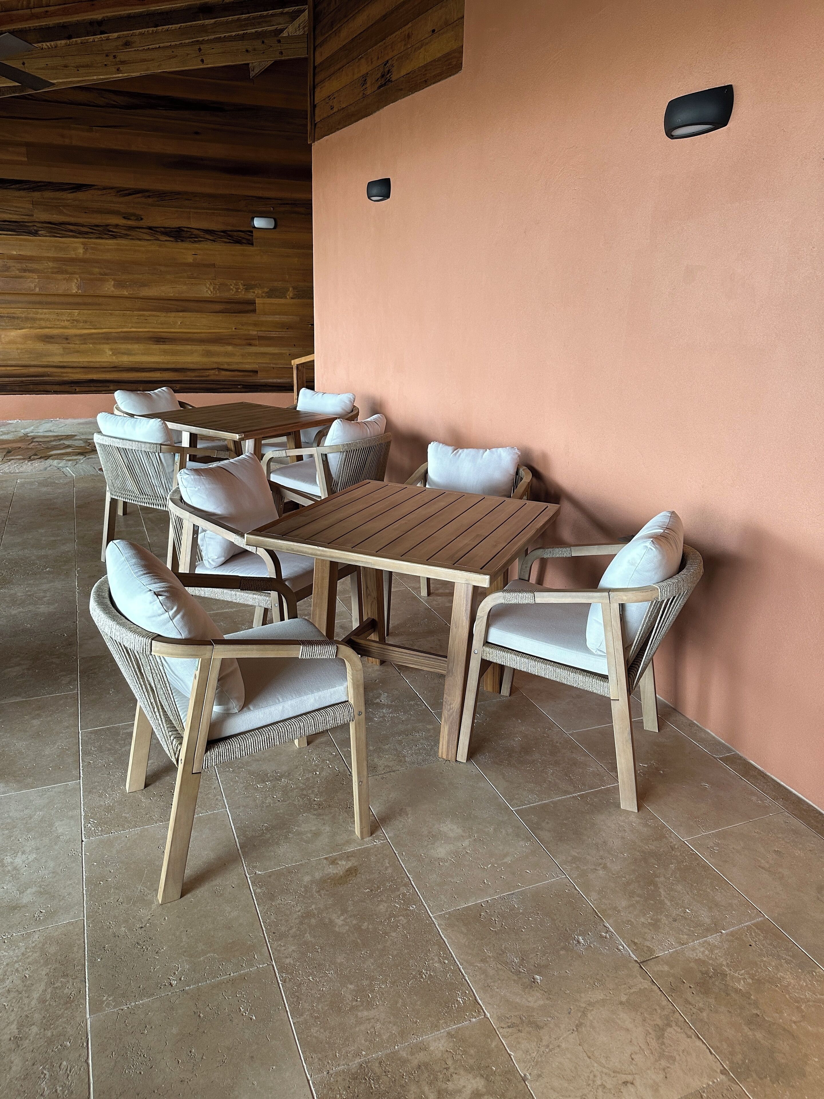 A wooden table and chairs set against a pink wall, with a tiled floor and wooden ceiling beams.