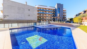 Un hotel moderno con piscina, un área exterior cubierta y un edificio de varios pisos con balcones.
