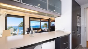 Una cocina moderna con una isla grande, muebles oscuros y vistas al océano.