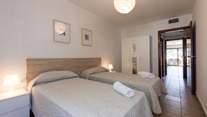 A hotel room with two beds, a wooden headboard, a nightstand with a lamp, and a door leading to a balcony. - Wake up to pool views · Festival Village (Salou)