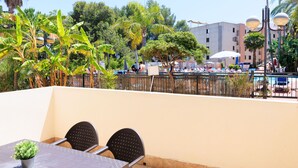 An outdoor seating area with a table and chairs, surrounded by palm trees and a fence. - Wake up to pool views · Festival Village (Salou)