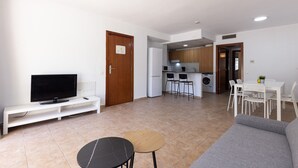 A modern living room with a flat-screen TV, a sofa, a small round table, and a dining area with chairs and a table. - Wake up to pool views · Festival Village (Salou)